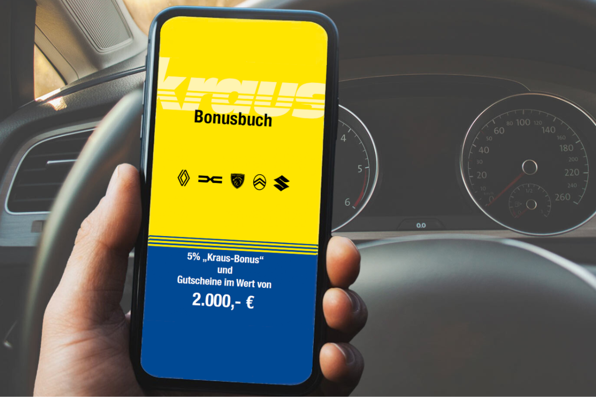 Eine Hand hält ein Handy und im Hintergrund ist ein Lenkrad zu erkennen
